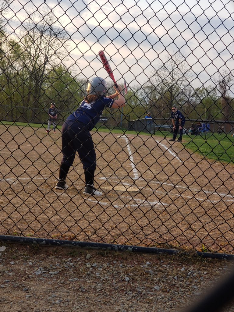 Rochester Area Youth Softball Association girl player athlete at bat on softball field with catcher ready to catch with All Kids Play financial assistance grant