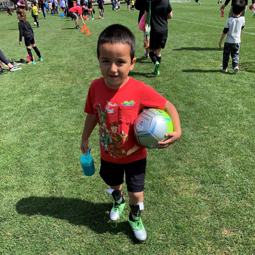 Male youth soccer player in California with ball, water bottle and in uniform on soccer field with All Kids Play financial assistance youth sports grant