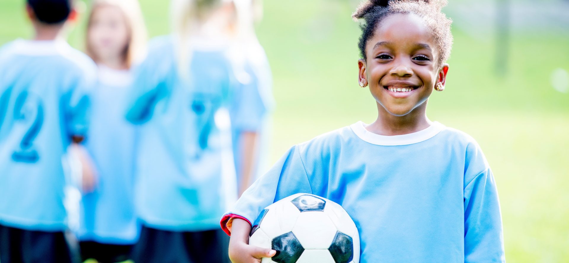 Youth female soccer athlete holding soccer ball on soccer field with team